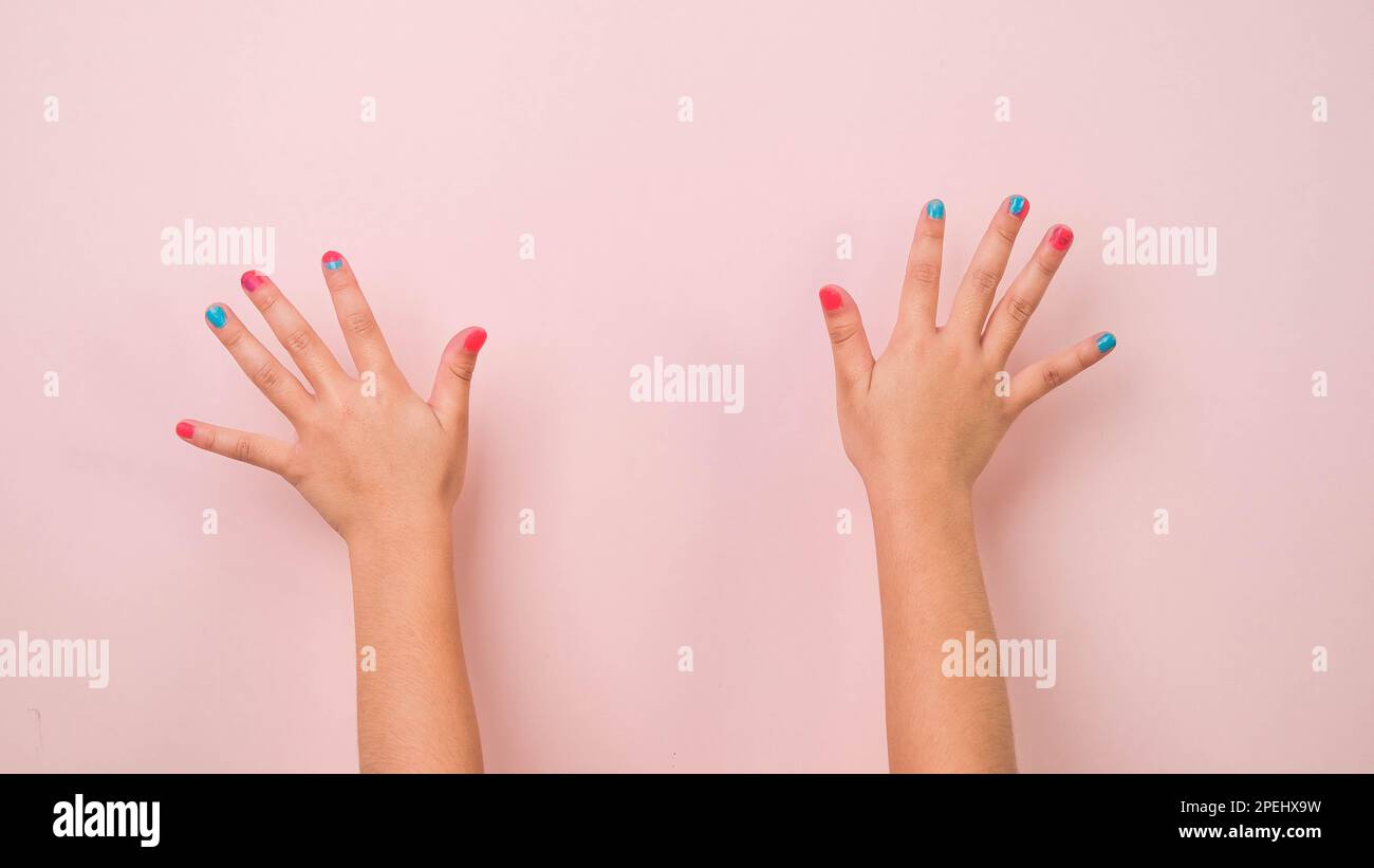 Primo piano della mano rialzata del bambino che mostra smalto per unghie su sfondo rosa pastello in studio. Pacchetto di movimenti di gesti e linguaggio del corpo. Foto Stock