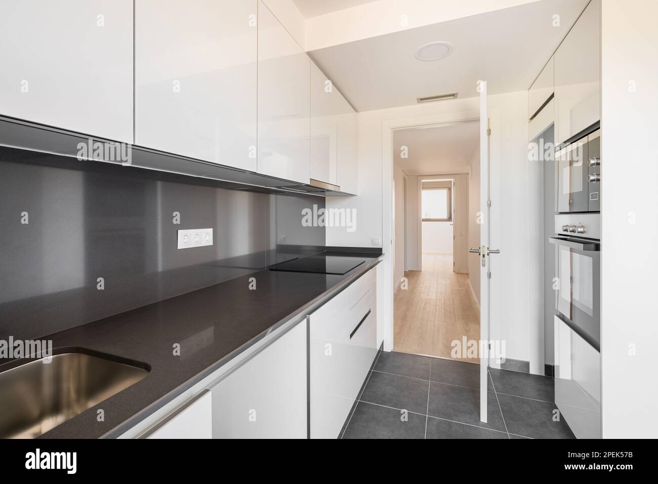 Moderna cucina high tech in bianco e nero con elettrodomestici e mobili moderni, con una porta aperta che si affaccia sul corridoio e una piccola camera con una finestra Foto Stock