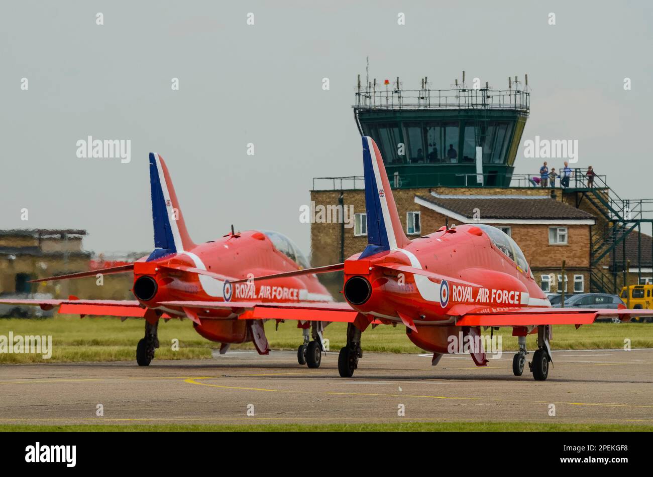 Royal Air Force Red Arrows mostra il team BAe Hawk T1 jet plane che si esibisce al RAF Scampton, con torre di controllo del traffico aereo. Guarda l'ufficio Foto Stock