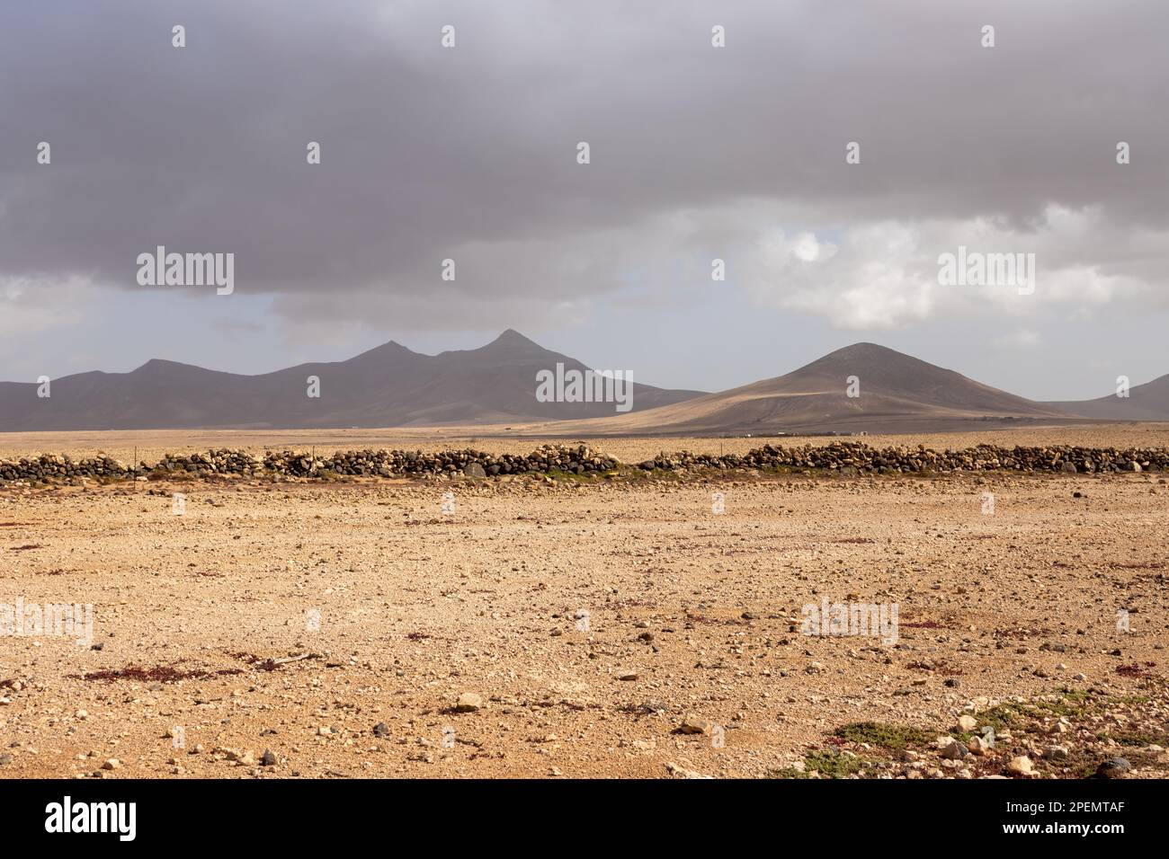 Colore giallo-marrone del terreno, pieno di pietre e rocce. Basso recinto fatto di loro. Silhouette di montagne sullo sfondo. Cielo nuvoloso nel wi Foto Stock