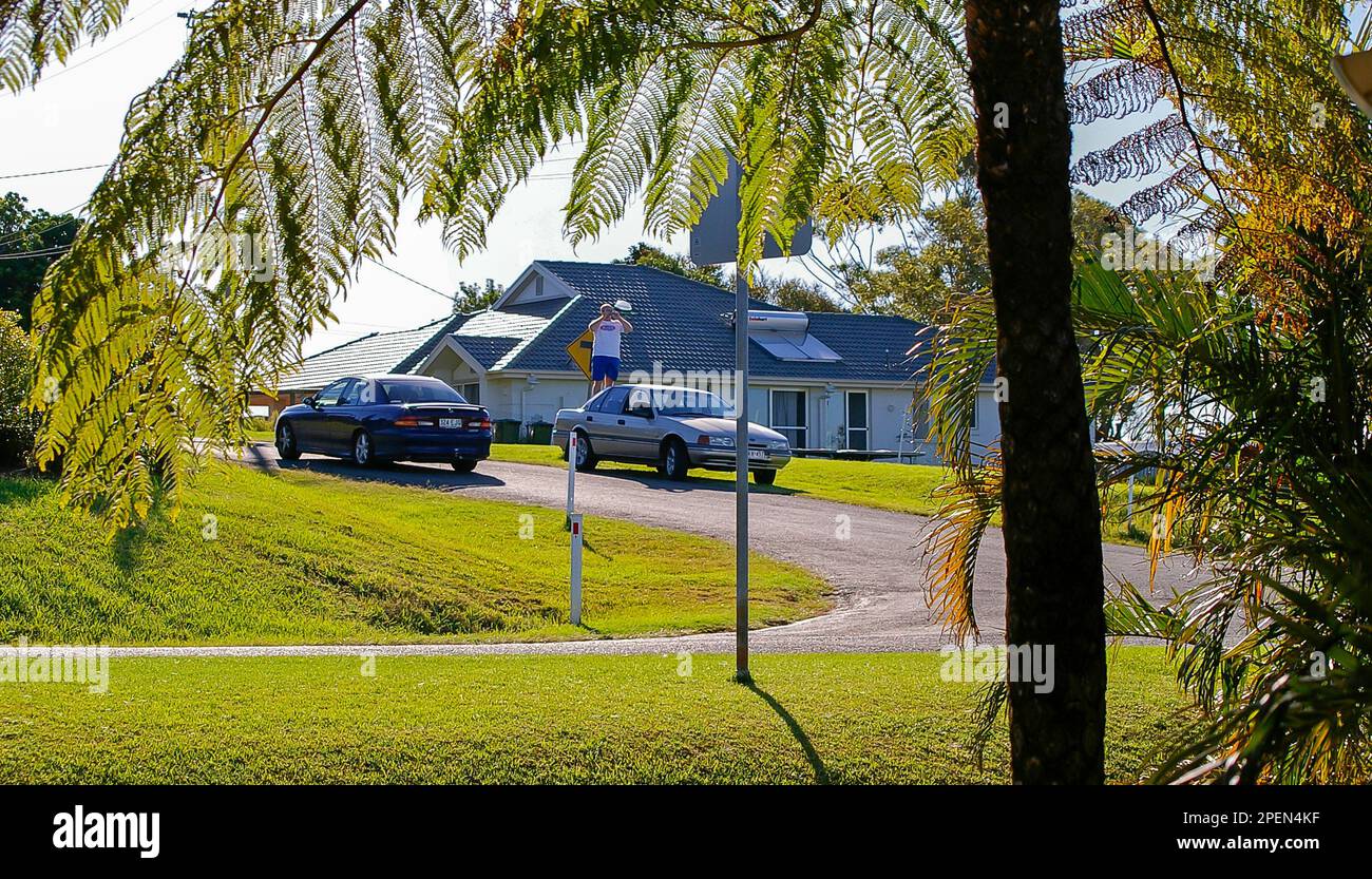 Un turista entusiasta che si trova sul retro di un'auto per fotografare la vista oltre le case vicine. Zona residenziale, Queensland meridionale, Australia Foto Stock