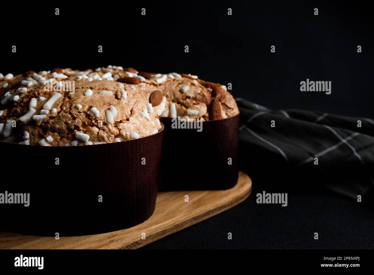 Torta di colomba di Pasqua, tagliere in legno, tovagliolo a righe su fondo di cemento scuro. Spazio di copia. Concetto di visualizzazione del prodotto o layout visivo chiave del design Foto Stock