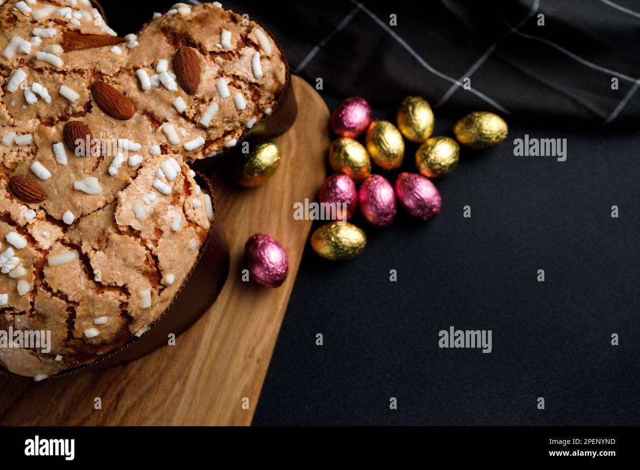 Torta di colomba di Pasqua, tagliere in legno, tovagliolo a righe su fondo di cemento scuro. Invito o messaggio di saluto. Spazio di copia. Tasto basso Foto Stock