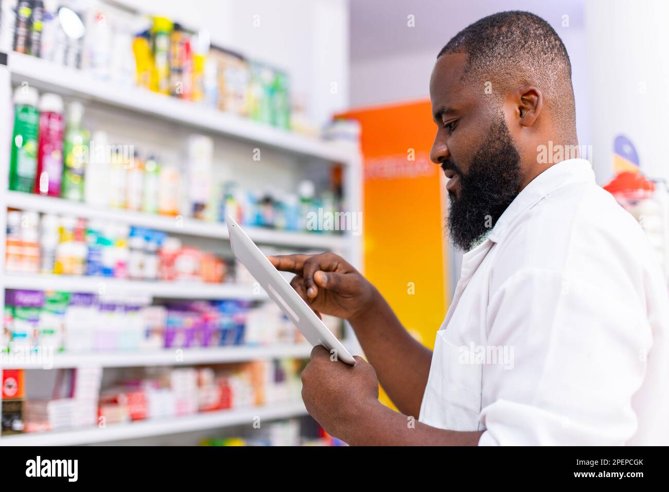 Ritratto del farmacista nero africano maschio utilizzando Smart Tablet per controllare l'inventario della medicina, prende scorta di prodotti per la salute. Foto Stock