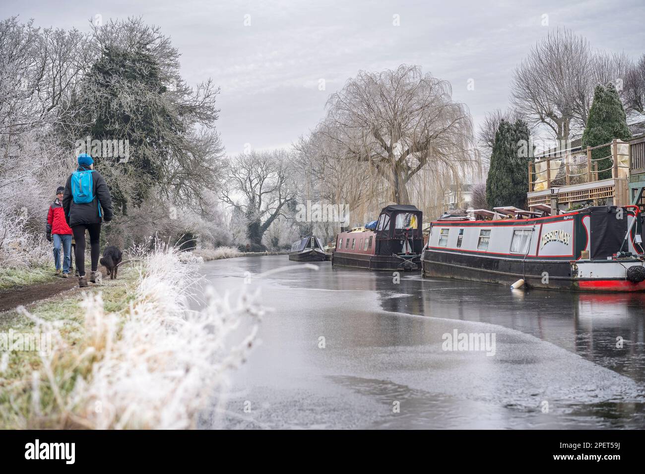 Mattinata fredda, ghiacciata e gelata sul canale britannico. Le barche sono ormeggiate su un lato, le persone camminano con il cane lungo il sentiero. Corsi d'acqua britannici congelati in inverno Foto Stock