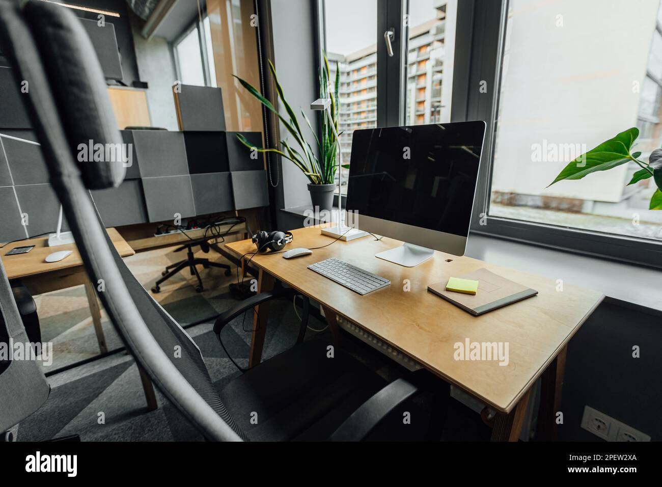 Una scrivania in un ufficio moderno con uno schermo sopra collocato contro una finestra di vetro Foto Stock