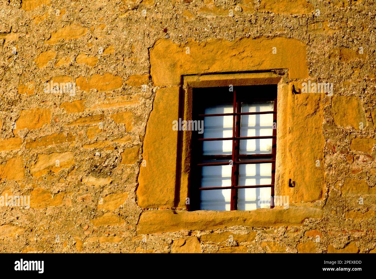 vecchio muro esterno in pietra gialla e finestra in legno marrone con tende bianche. superficie stucco in stucco. muratura deteriorante. grana sabbiosa. Foto Stock
