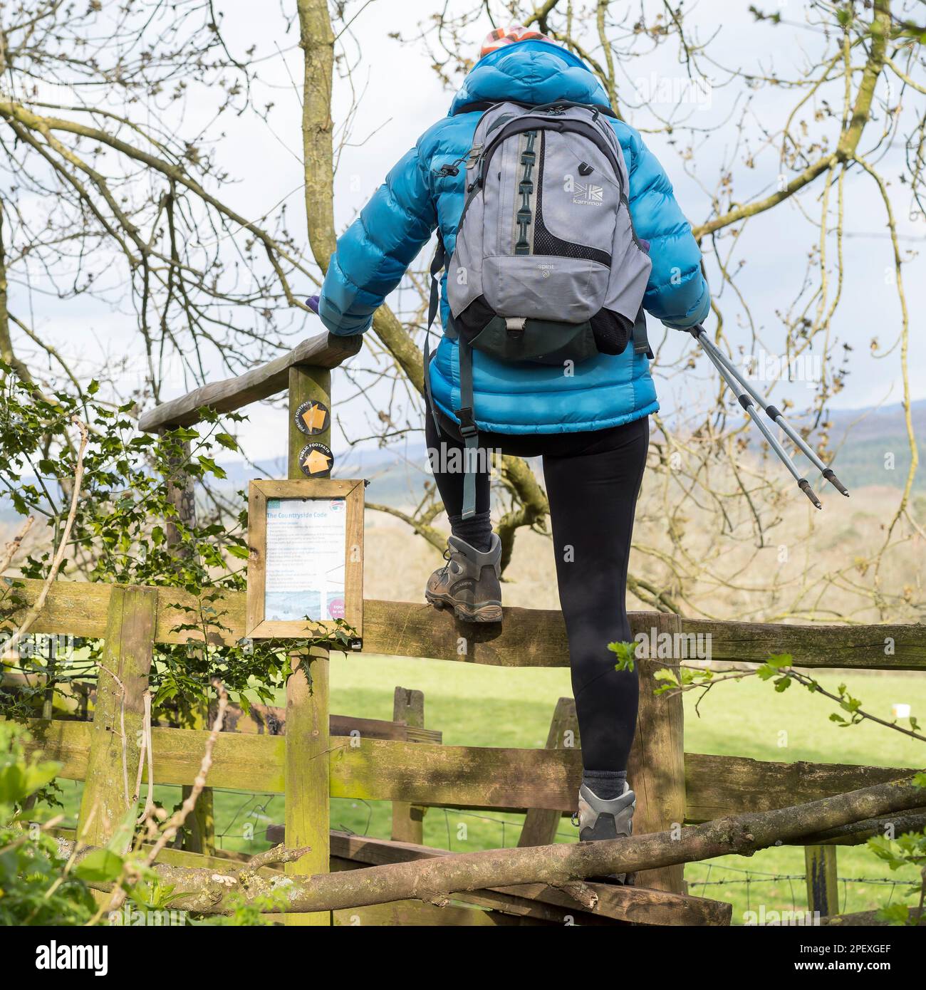 Il codice campagna è riportato su un posto nella campagna del Regno Unito. Una donna escursionista si arrampica sullo stile accanto al cartello. Foto Stock
