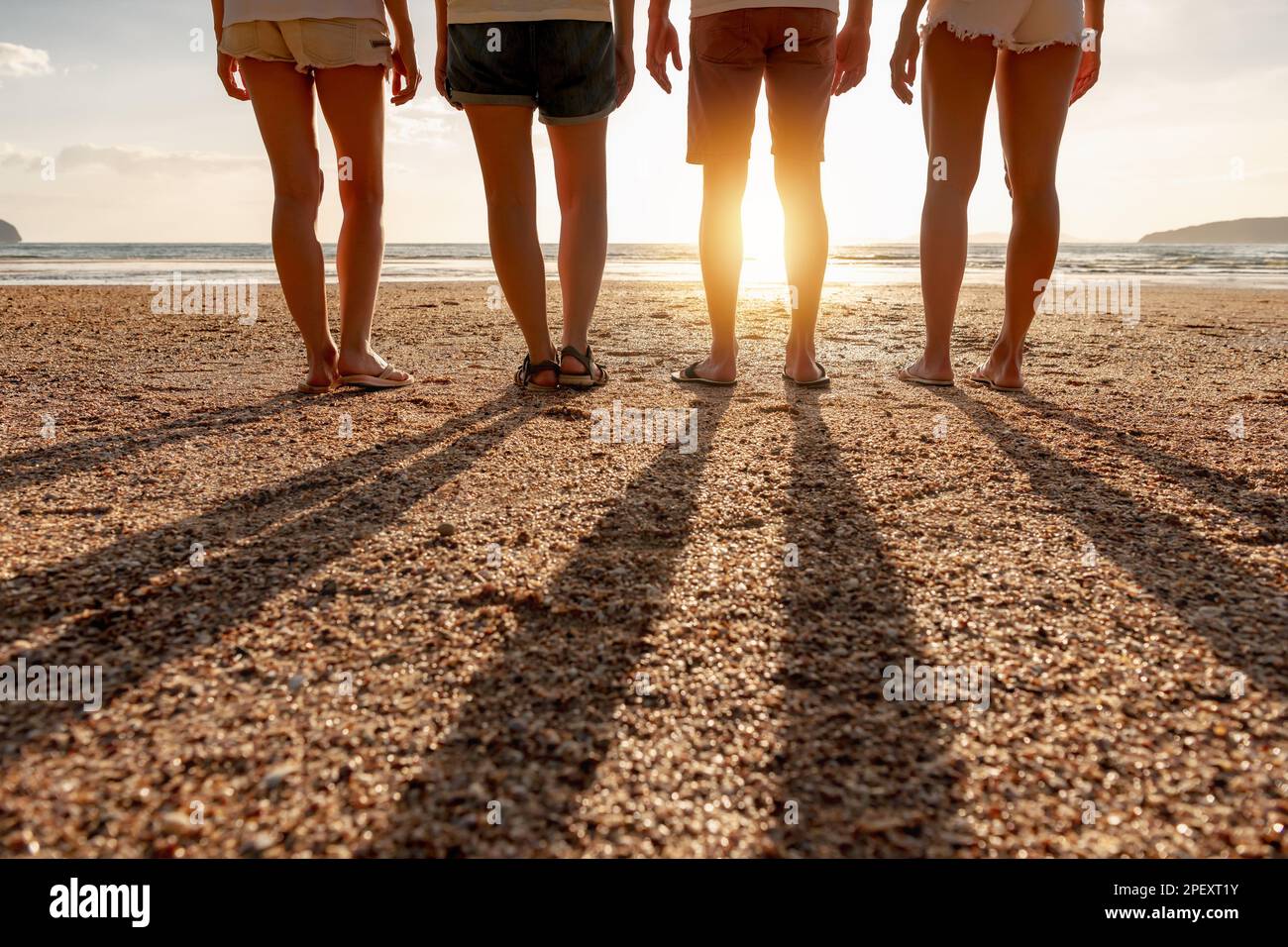 Gruppo di amici si trova al tramonto spiaggia di mare. Foto in primo piano di gambe e ombre lunghe Foto Stock