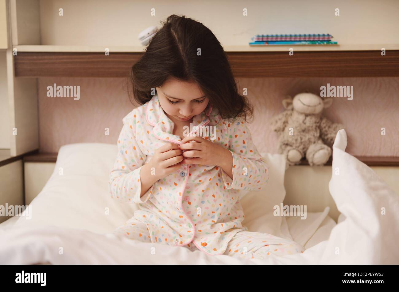Affascinante bambina bottoni sul suo pigiama, si siede a letto e si prepara per il letto. Il concetto di andare a letto e svegliarsi Foto Stock