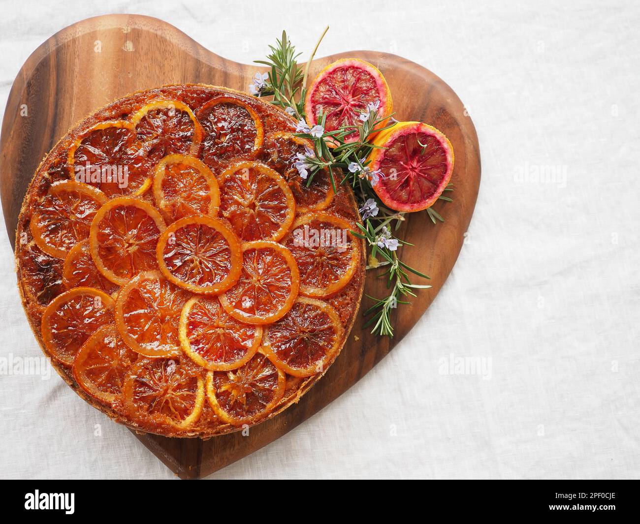 Torta rovesciata di arancia rossa e contorno rosmarino sparato dall'alto su un piano di servizio a forma di cuore su sfondo bianco con spazio per la copia Foto Stock