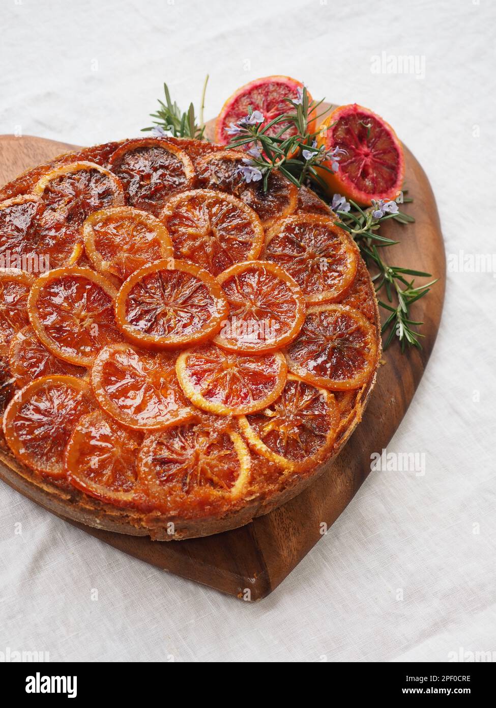 Primo piano di un'appetitosa torta rovesciata di arancia rossa su una tagliera a forma di cuore su una tovaglia di lino bianco Foto Stock