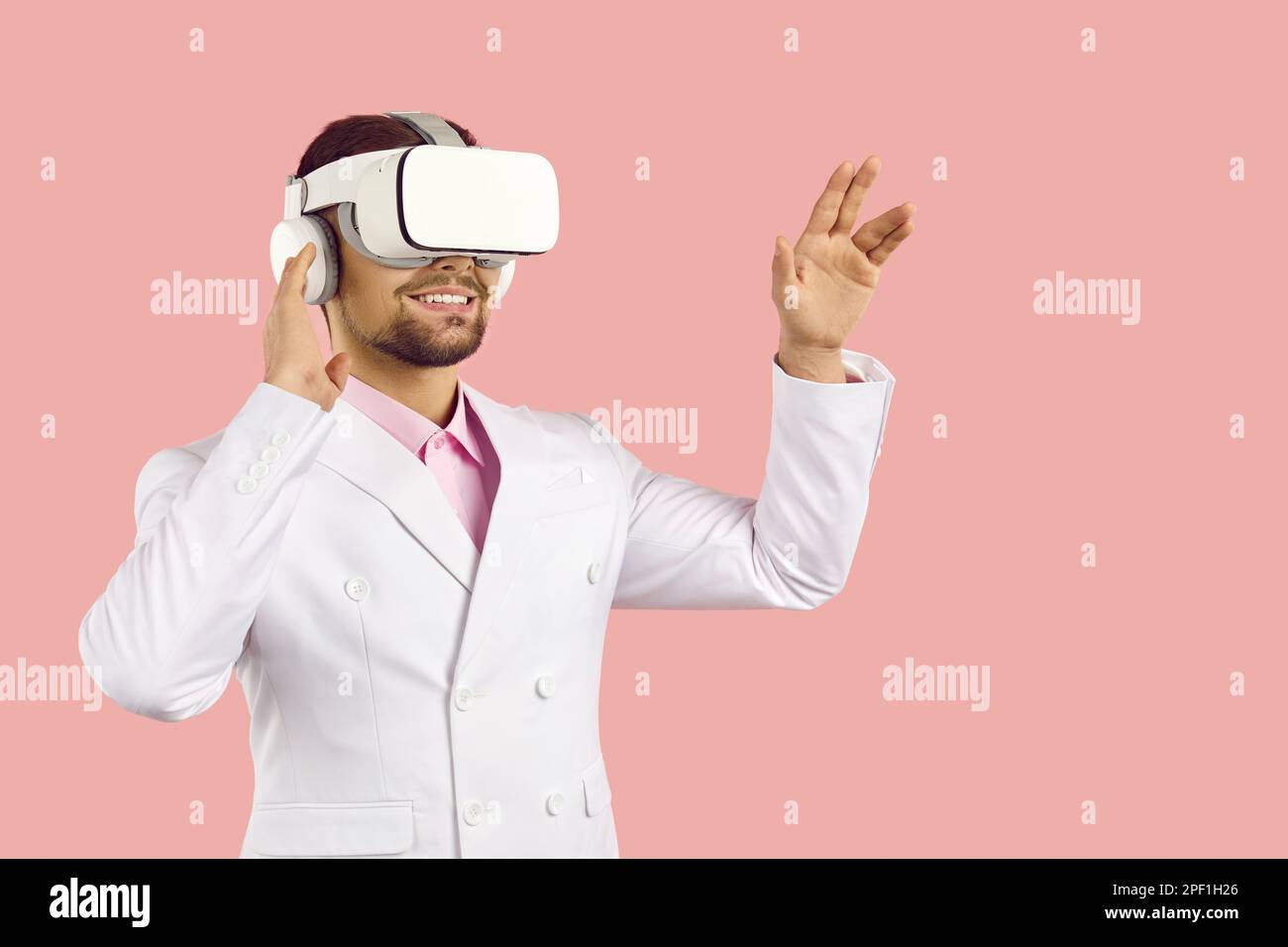 Giovane uomo sorridente che indossa occhiali per realtà virtuale isolati su sfondo rosa pastello. Foto Stock