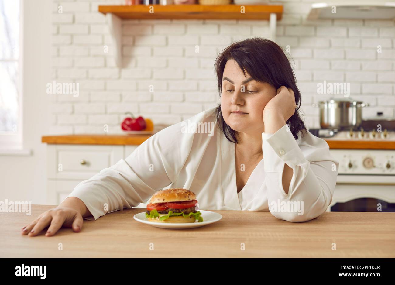 Giovane donna in sovrappeso che esita a mangiare hamburger enorme Foto Stock