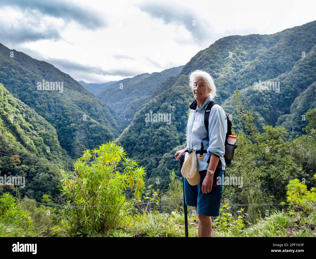 Una donna che cammina lungo la Levada da Janella sopra Ribieras da Janella su Madeira con la foresta nativa di Laurel. Foto Stock