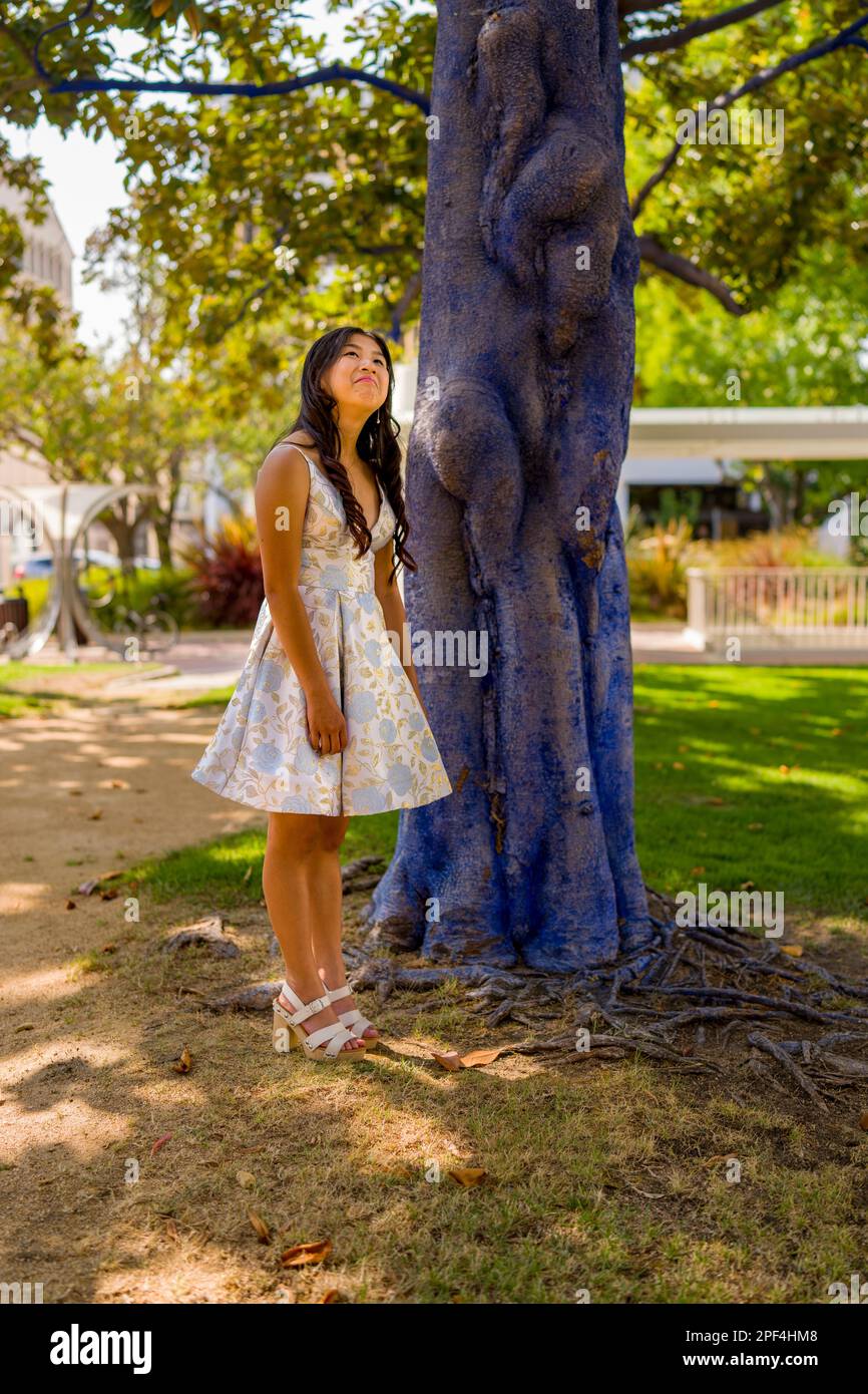 Ragazza adolescente in Prom Dress in piedi vicino dipinto albero blu con un look premuroso | pomeriggio | Abito corto | Petite Foto Stock