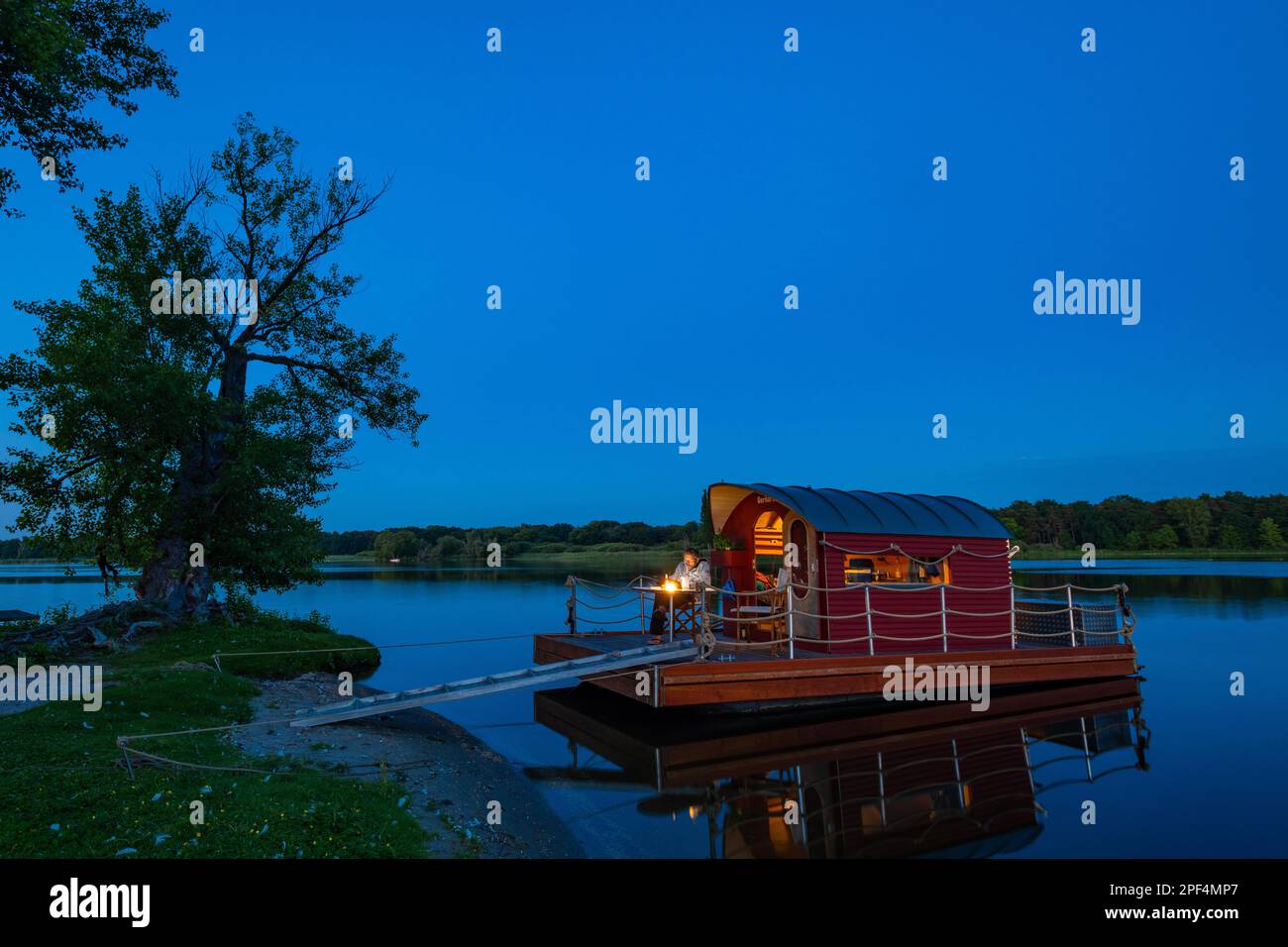 Uomo seduto nell'ora blu su una casa galleggiante, zattera casa, di fronte all'isola Kiehnwerder, Breitlingsee, Brandenburgo an der Havel, Havelland Foto Stock