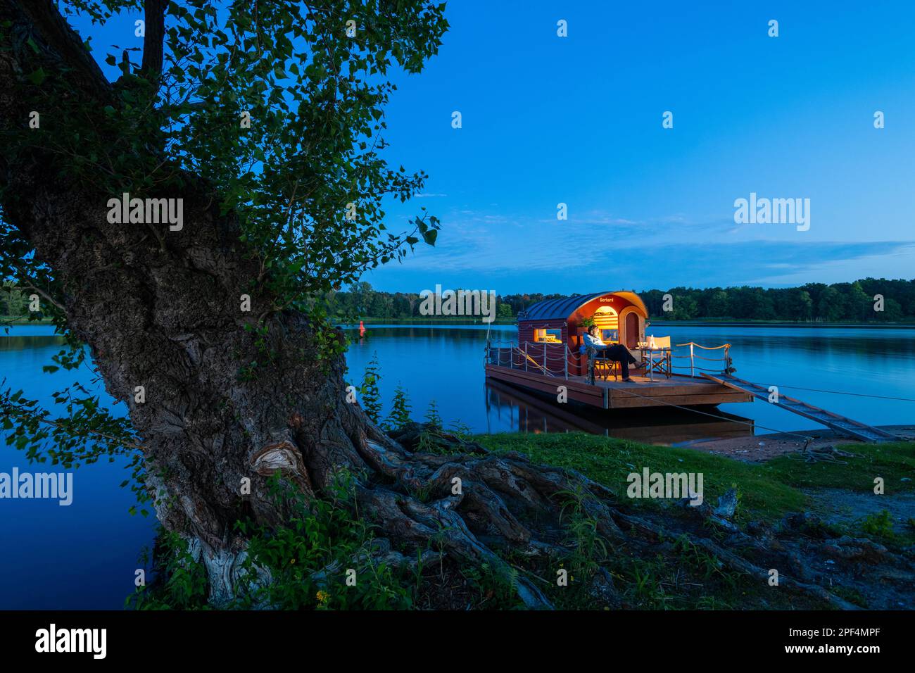 Uomo seduto nell'ora blu su una casa galleggiante, zattera casa, di fronte all'isola Kiehnwerder, Breitlingsee, Brandenburgo an der Havel, Havelland Foto Stock