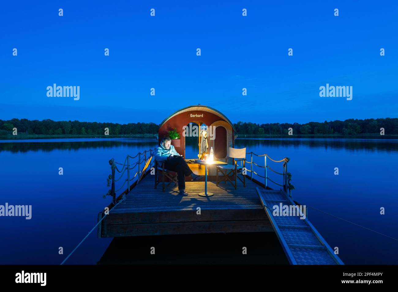 Uomo seduto nell'ora blu su una casa galleggiante, zattera casa, di fronte all'isola Kiehnwerder, Breitlingsee, Brandenburgo an der Havel, Havelland Foto Stock