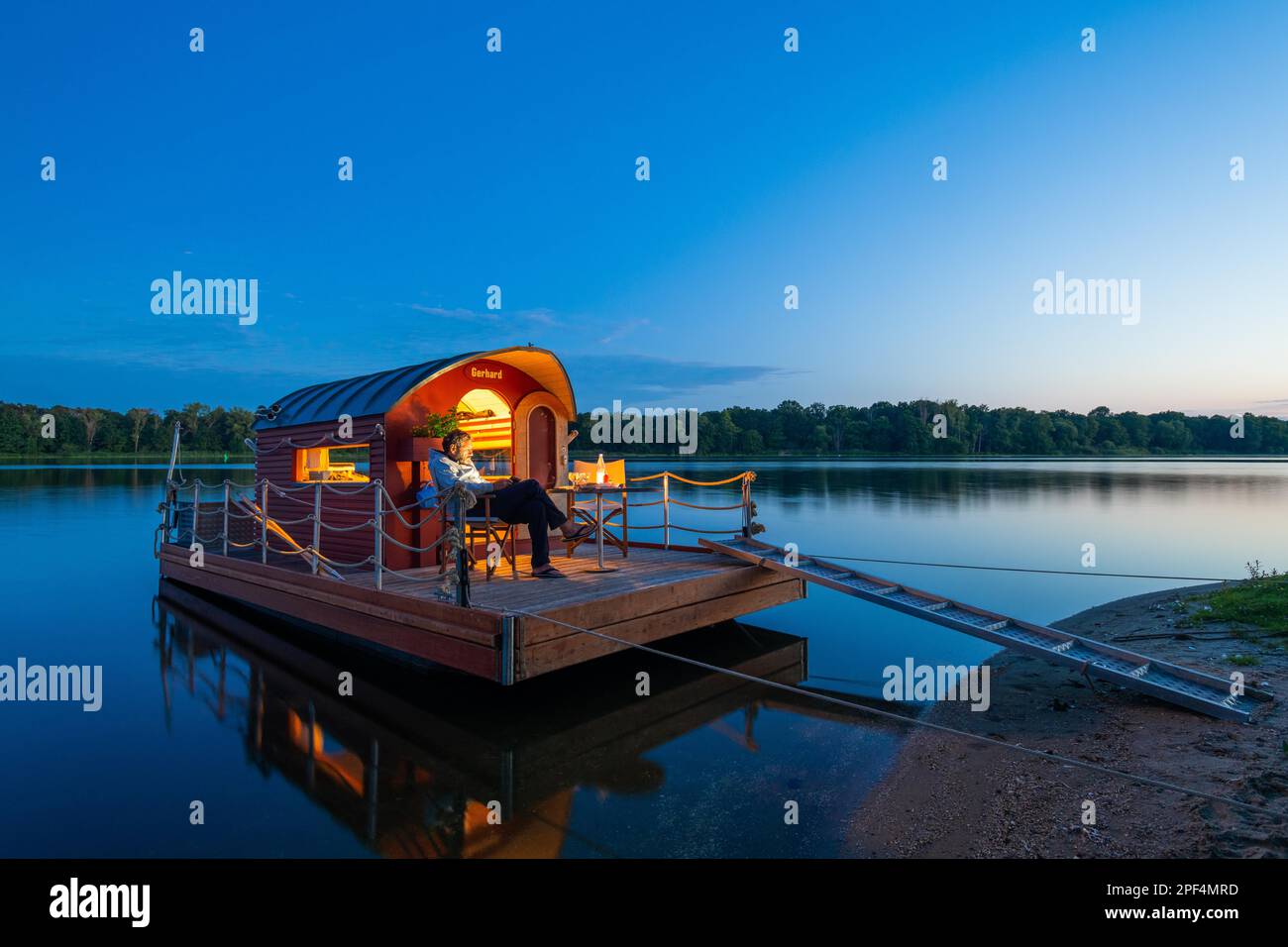 Uomo seduto nell'ora blu su una casa galleggiante, zattera casa, di fronte all'isola Kiehnwerder, Breitlingsee, Brandenburgo an der Havel, Havelland Foto Stock