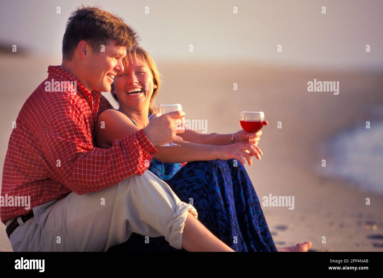 Giovane coppia caucasica godendo un bicchiere di vino ben seduti a piedi nudi sulla spiaggia Foto Stock