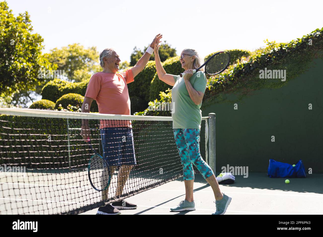 Amici anziani caucasici felici con racchette da tennis alta fiving al campo da tennis nella giornata di sole Foto Stock