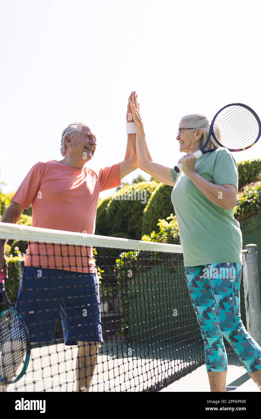 Felice caucasico anziani amici in alto fiving a campo da tennis il giorno di sole, copia spazio Foto Stock