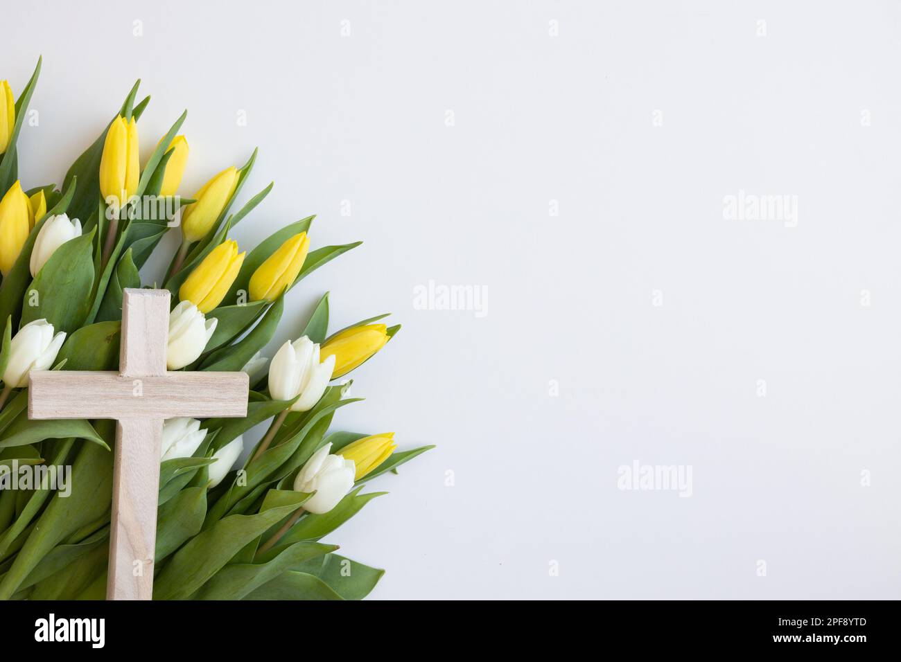 Semplice croce cristiana in legno con tulipani gialli e bianchi su sfondo bianco con spazio copia Foto Stock