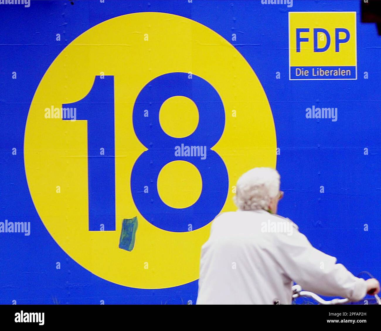 An elderly woman pushes her bicycle past an election poster of the German Liberal Democratic Party (FDP) in Duisburg, western Germany, Saturday, Sept. 21, 2002, one day ahead of the general elections in Germany on Sunday, Sept. 22nd. The big 18 refers to the party's aim to win 18 percent of the votes as an unidentified person had painted a decimal point between the one and eight. (AP Photo/Frank Augstein) Foto Stock