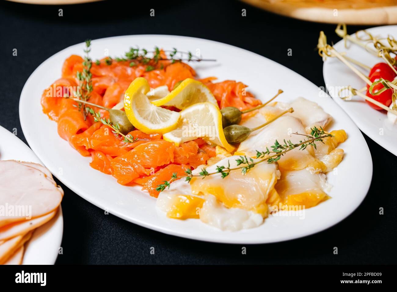 Filetti a fette di pesce grasso. Salmone affumicato con fettine di limone e filetti di ippoglosso con capperi grandi. Prodotto utile ricco di omega-3. Foto Stock