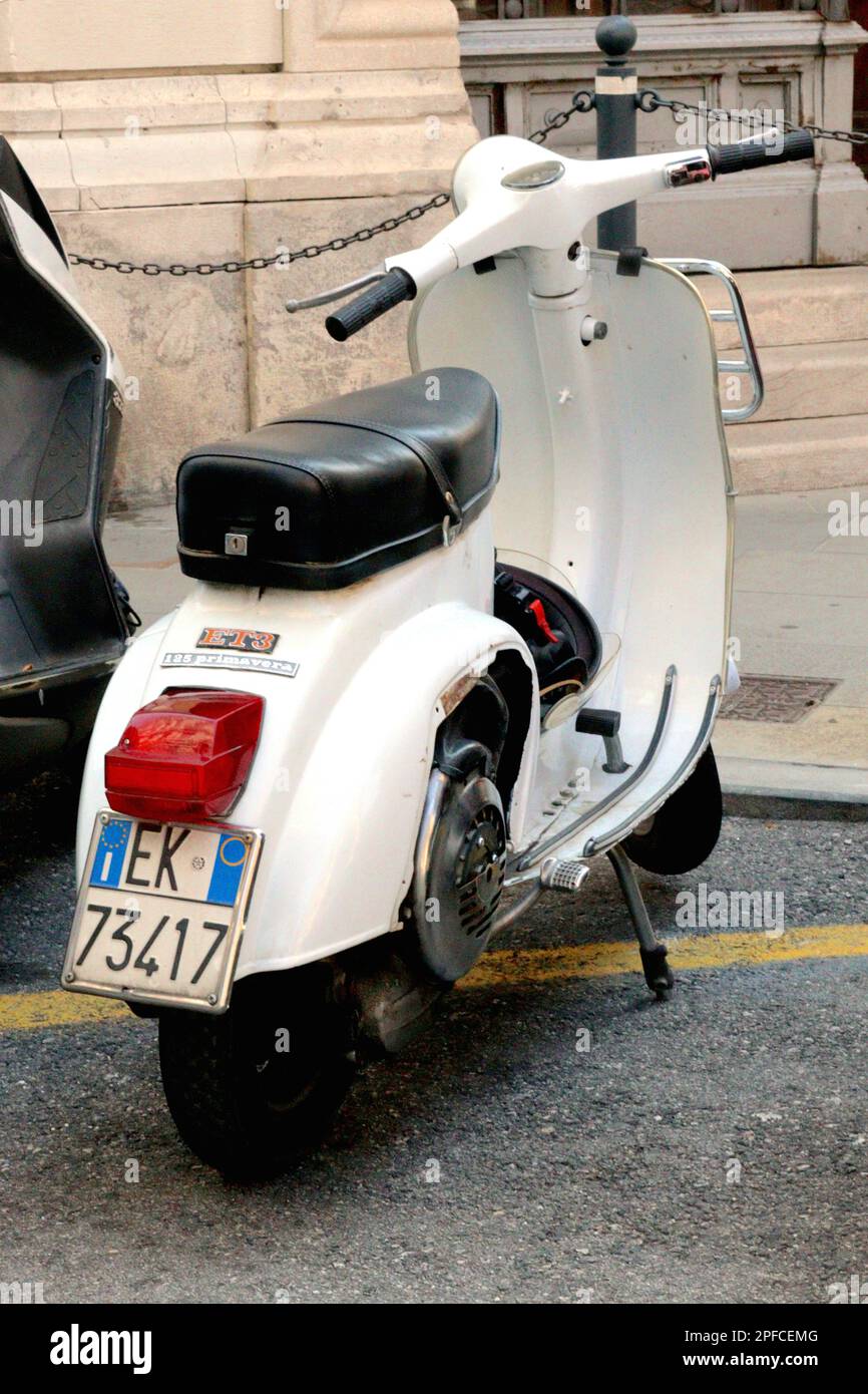 Un'icona italiana, una Vespa 125cc ET3 Primavera smallframe parcheggiata in una baia di moto popolata di auto, ciclomotori e motociclette, Trieste Italia. Foto Stock
