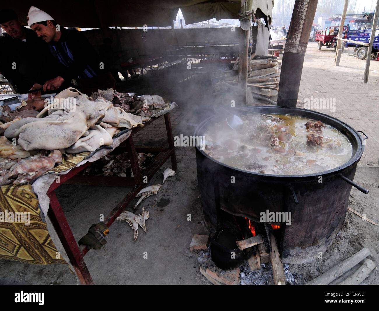 Bollire la carne di montone in una grande pentola sopra il fuoco di legno in un ristorante in un mercato settimanale del bestiame nella periferia di Kashgar, Xinjiang, Cina. Foto Stock