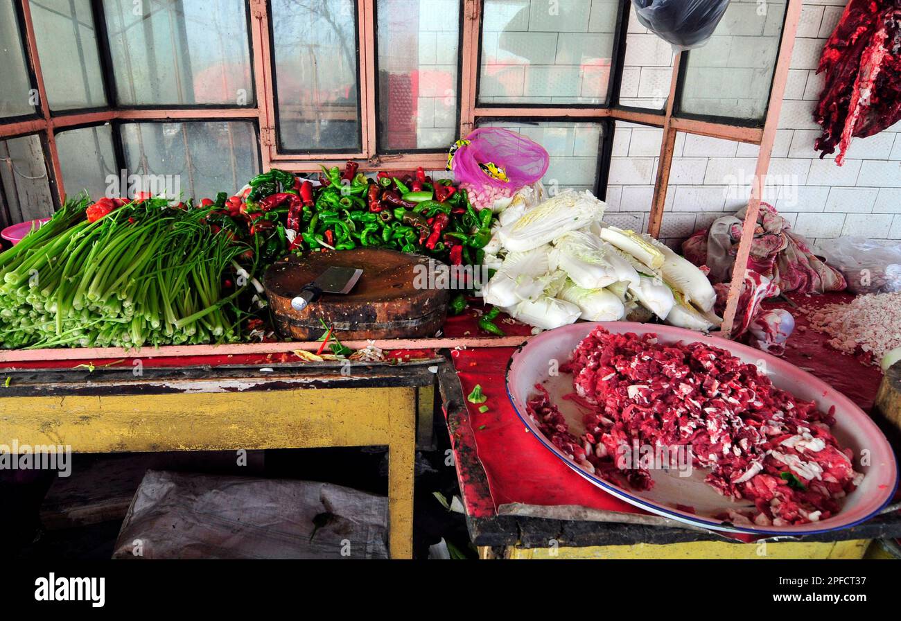 Carne fresca di agnello, peperoncini e verdure in un cucinino di un piccolo ristorante sulla strada in un mercato nella periferia di Kashgar, Xinjiang, Cina. Foto Stock