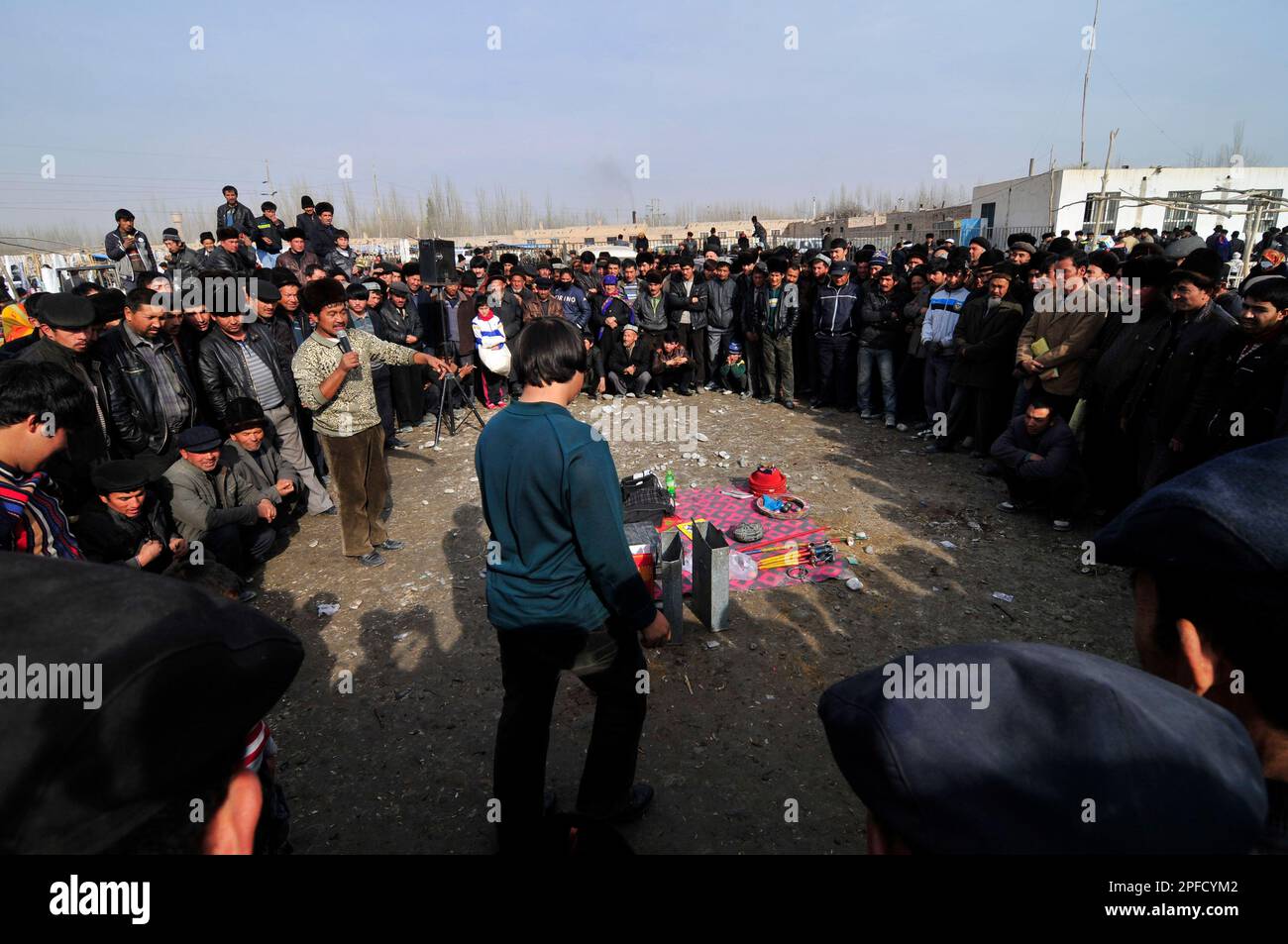 Uomini Uyghur che guardano uno spettacolo di un esecutore in un mercato locale settimanale nella periferia di Kashgar, Xinjiang, Cina. Foto Stock