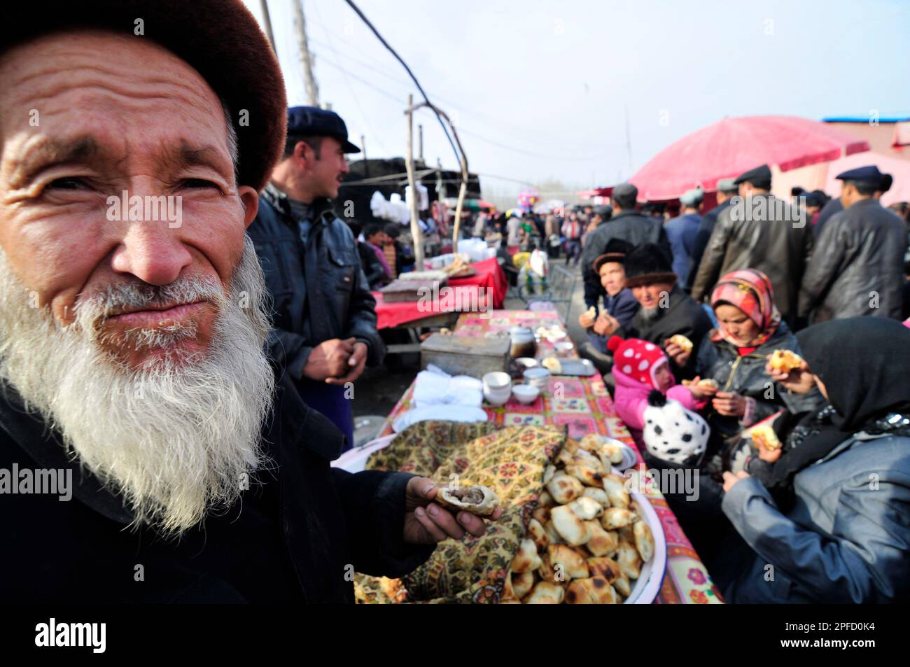 Un anziano uomo Uighur che mangia Samsa - un tradizionale tandoor forno pasta ripiena di carne. Foto Stock