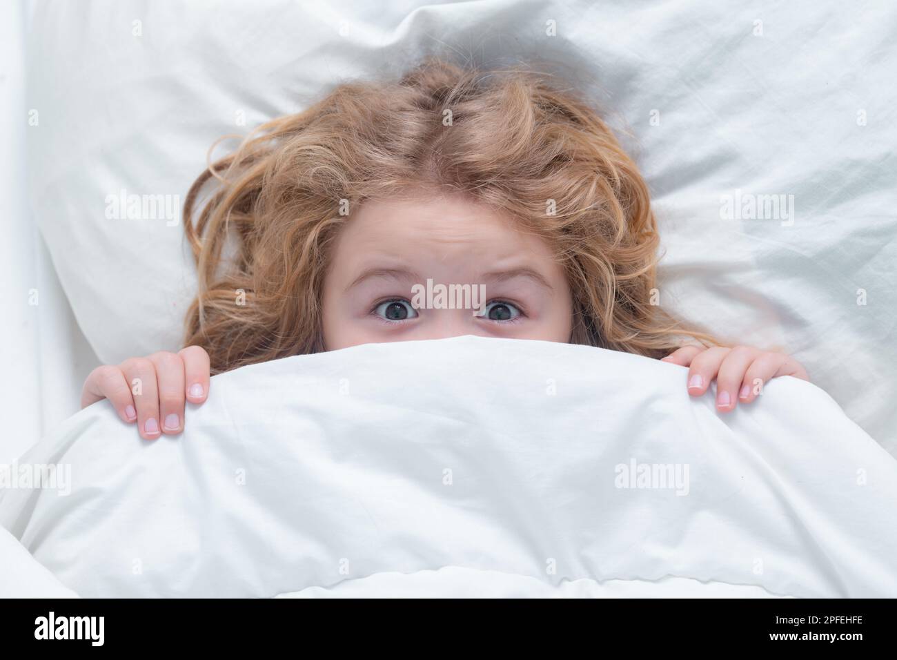 Ragazzo spaventato che si nasconde a letto. Copriletto per bambini,  copriletto con coperta. Bambino sdraiato a letto, sveglia. Risveglio  mattutino, soleggiata camera per bambini. Incubo Foto stock - Alamy