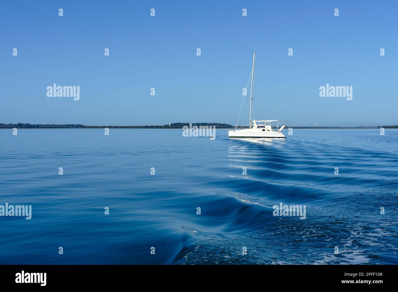 Le increspature del lavaggio dietro una barca conducono l'occhio ad una singola barca bianca sulle calme acque blu in mare aperto all'isola di Coochiemudlo Foto Stock