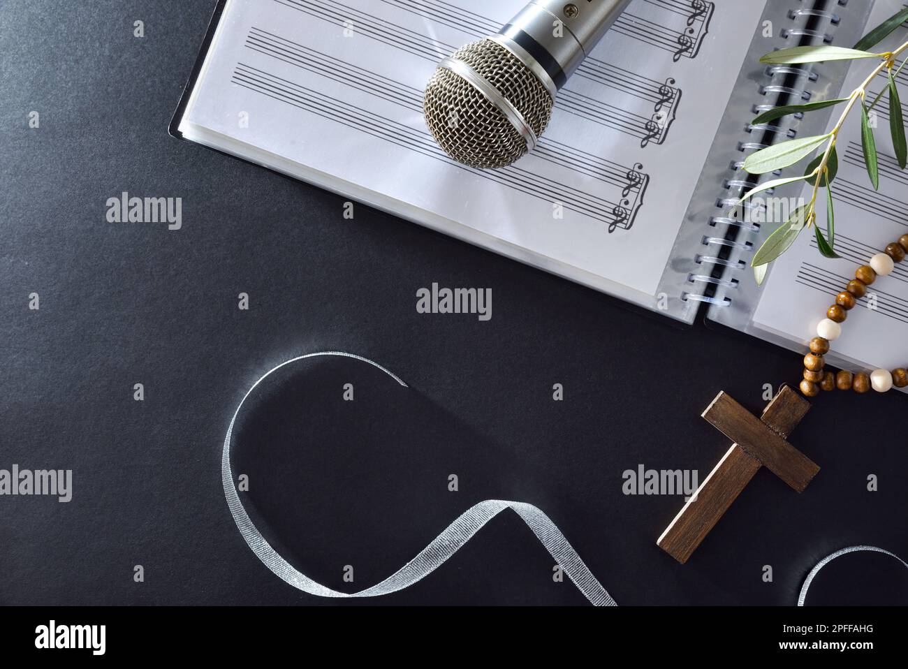 Sottofondo musicale corale per la Domenica delle Palme con spartiti, microfono e rami di ulivo con croce cristiana su un tavolo nero. Vista dall'alto. Foto Stock