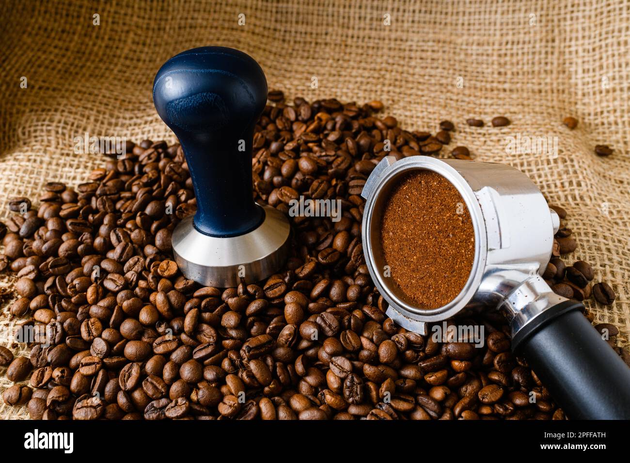 Caffè fondo in chicchi tostati interi con supporto in metallo e legno e manomissioni su sackcloth, strumenti professionali per baristi Foto Stock