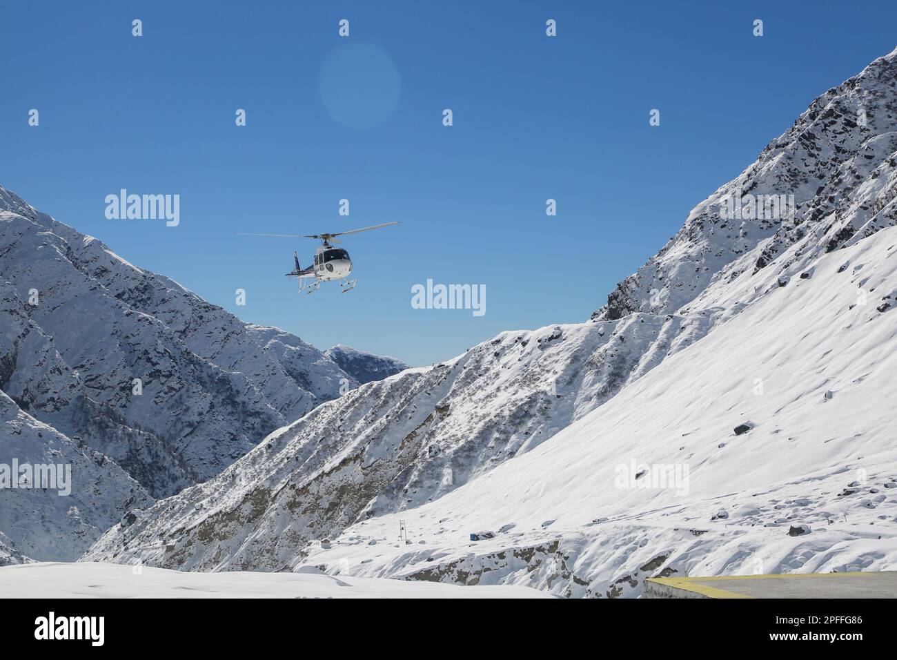 Elicottero che vola nella valle innevata della montagna in Himalaya. Elicottero bianco su un paesaggio bianco con sfondo cielo blu chiaro. Foto Stock