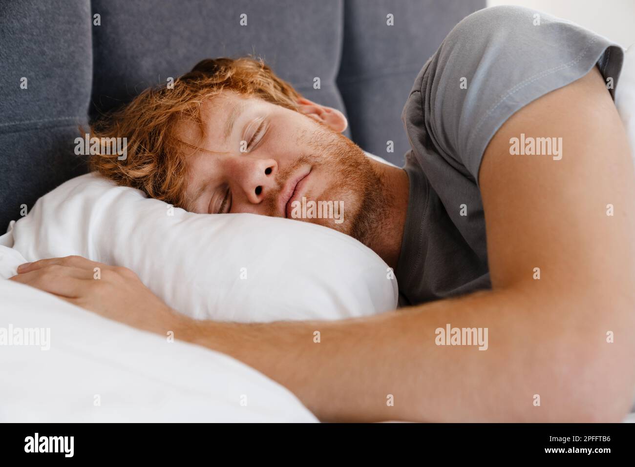Ritratto di giovane bell'uomo dormiente rosso in t-shirt grigia a letto a casa Foto Stock
