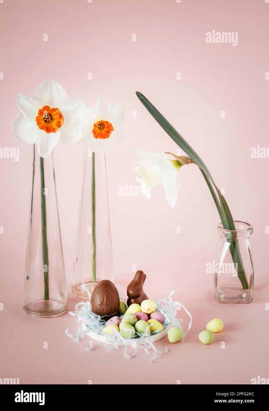 Natura morta di Pasqua con narcisi in vasi di vetro, uova di pasqua e mini coniglietto di cioccolato Foto Stock