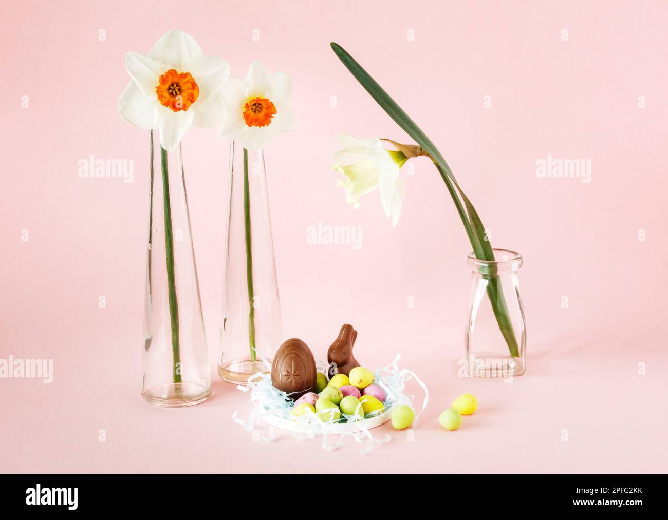 Natura morta di Pasqua con tre narcisi in vasi di vetro, uova di pasqua e mini coniglietto di cioccolato Foto Stock