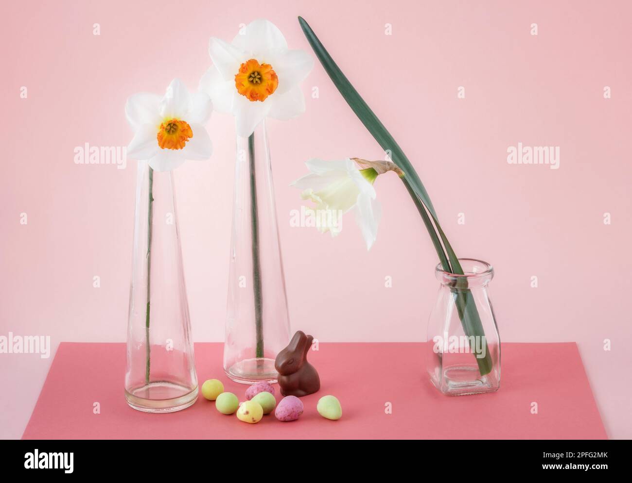 Natura morta pasquale con tre narcisi in vasi di vetro e dolci Foto Stock
