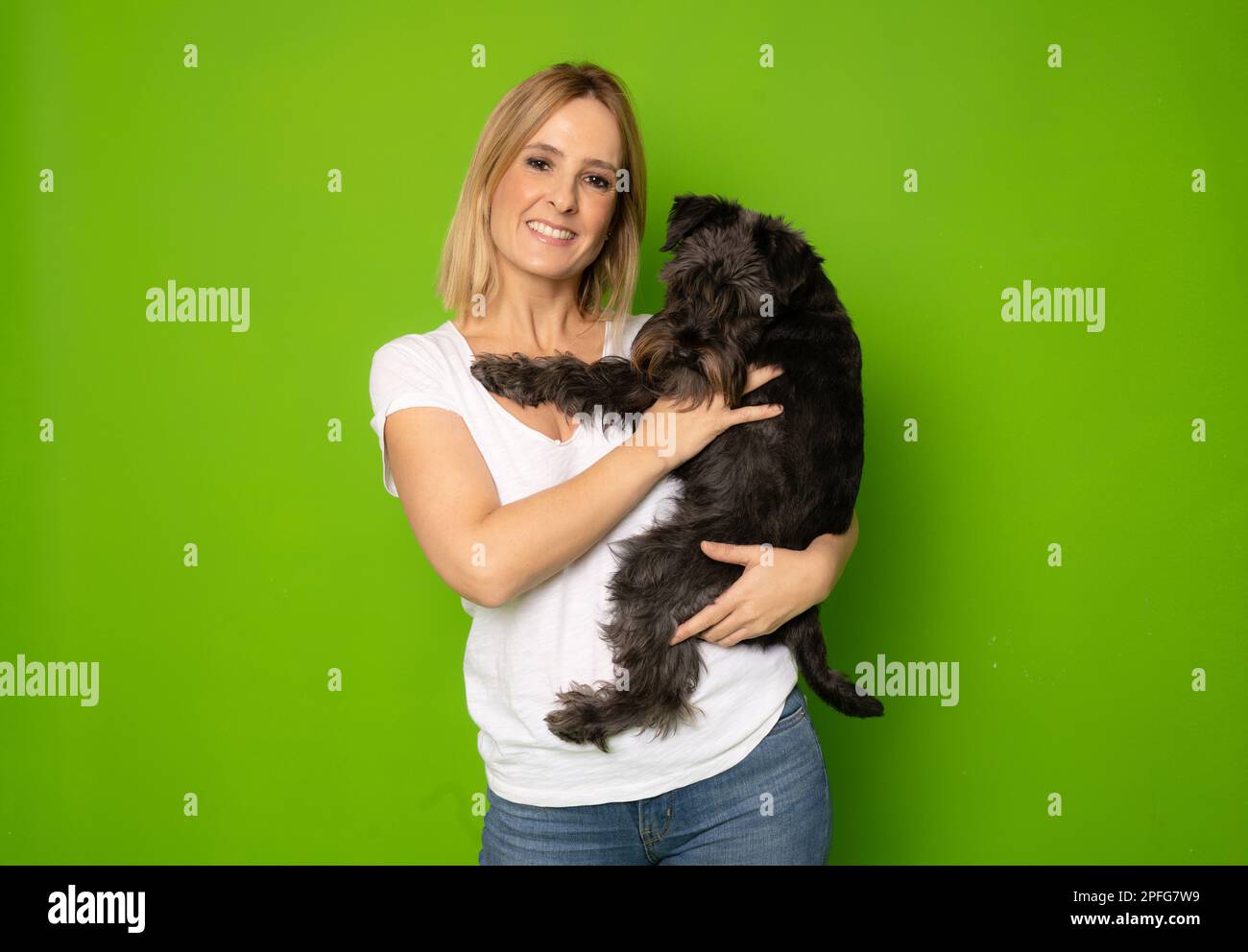 Ritratto di bella ragazza allegra attenta che tiene in mano schnauzer doggy isolato su sfondo di colore verde brillante Foto Stock