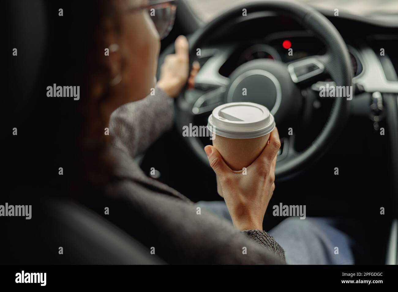 Primo piano di una giovane donna che beve caffè da togliere durante la guida per lavorare in auto Foto Stock