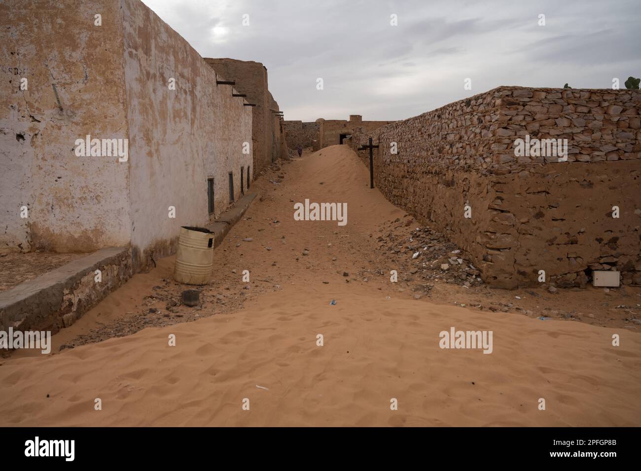 Una strada stretta nell'antica città di Chinguetti, Mauritania, fiancheggiata da edifici storici in pietra, con le sabbie desertiche che invadono. Foto Stock