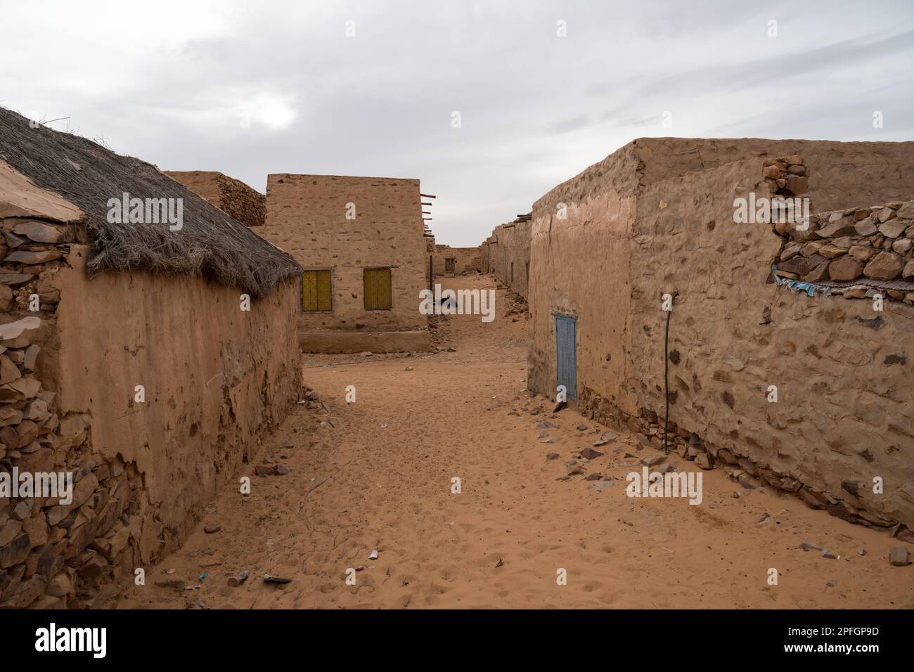 Una strada stretta nell'antica città di Chinguetti, Mauritania, fiancheggiata da edifici storici in pietra, con le sabbie desertiche che invadono. Foto Stock
