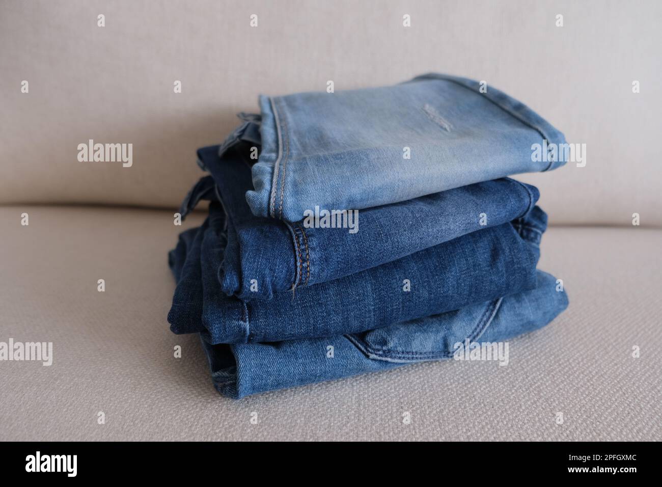 Quattro pantaloni denim, pantaloni denim ripiegati e impilati su un divano bianco, foto idea in tessuto denim. Foto Stock