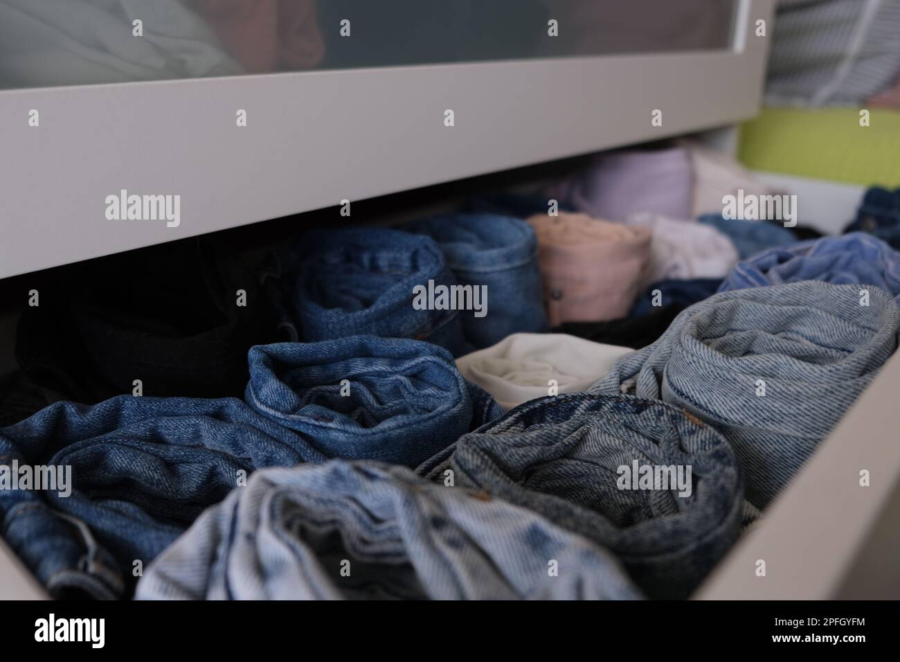 Cassettiera pila di pantaloni in denim, cassetto quasi aperto con jeans in denim arrotolati all'interno, primo piano. Messa a fuoco selettiva. Concetto di denim foto idea. Foto Stock
